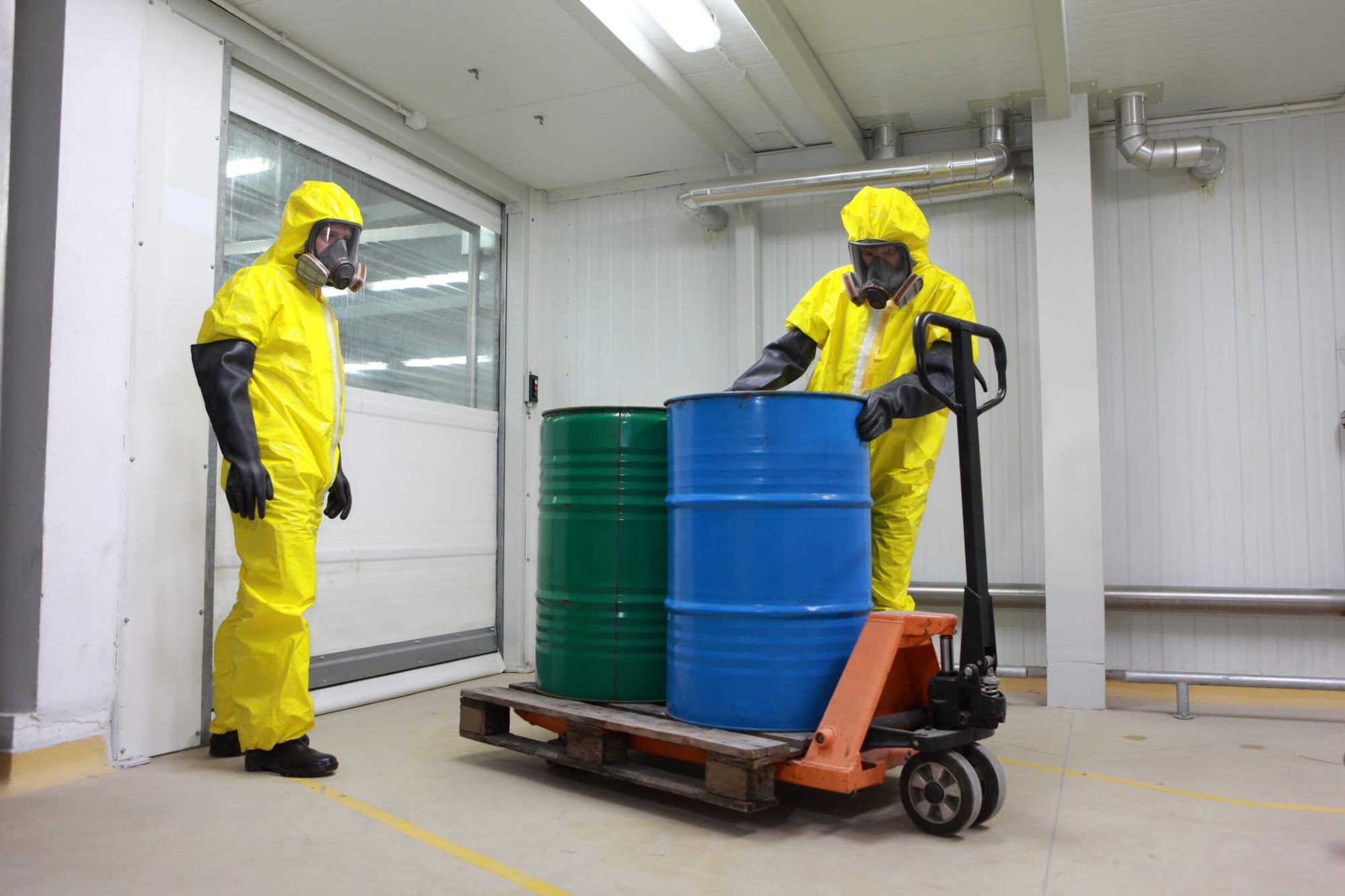 Two workers in hazmat suits handling barrels of chemicals
